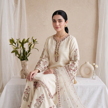 Woman in a cream embroidered traditional outfit sitting on a white draped background